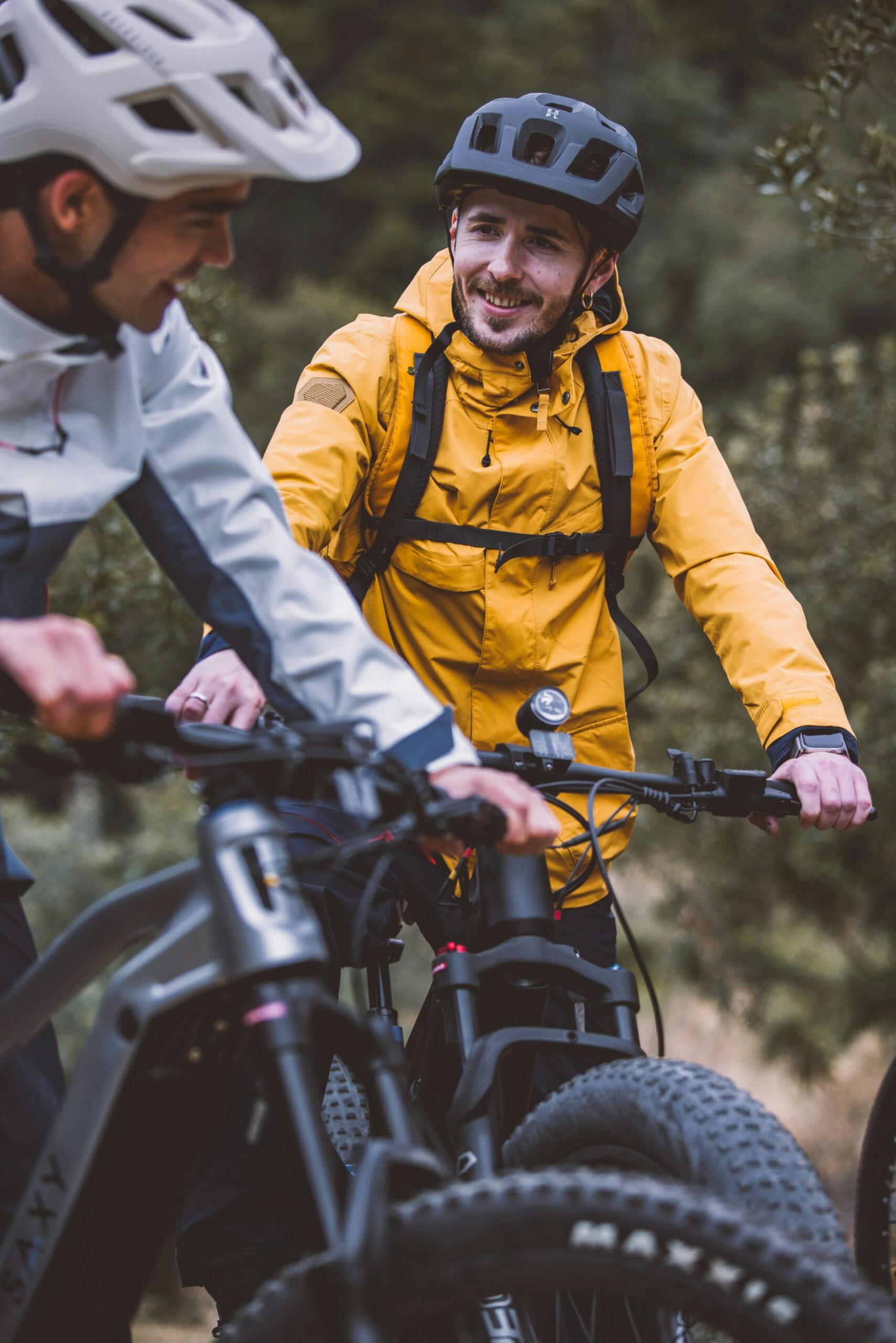Two men mountain biking with safety helmets and jackets, enjoying nature.